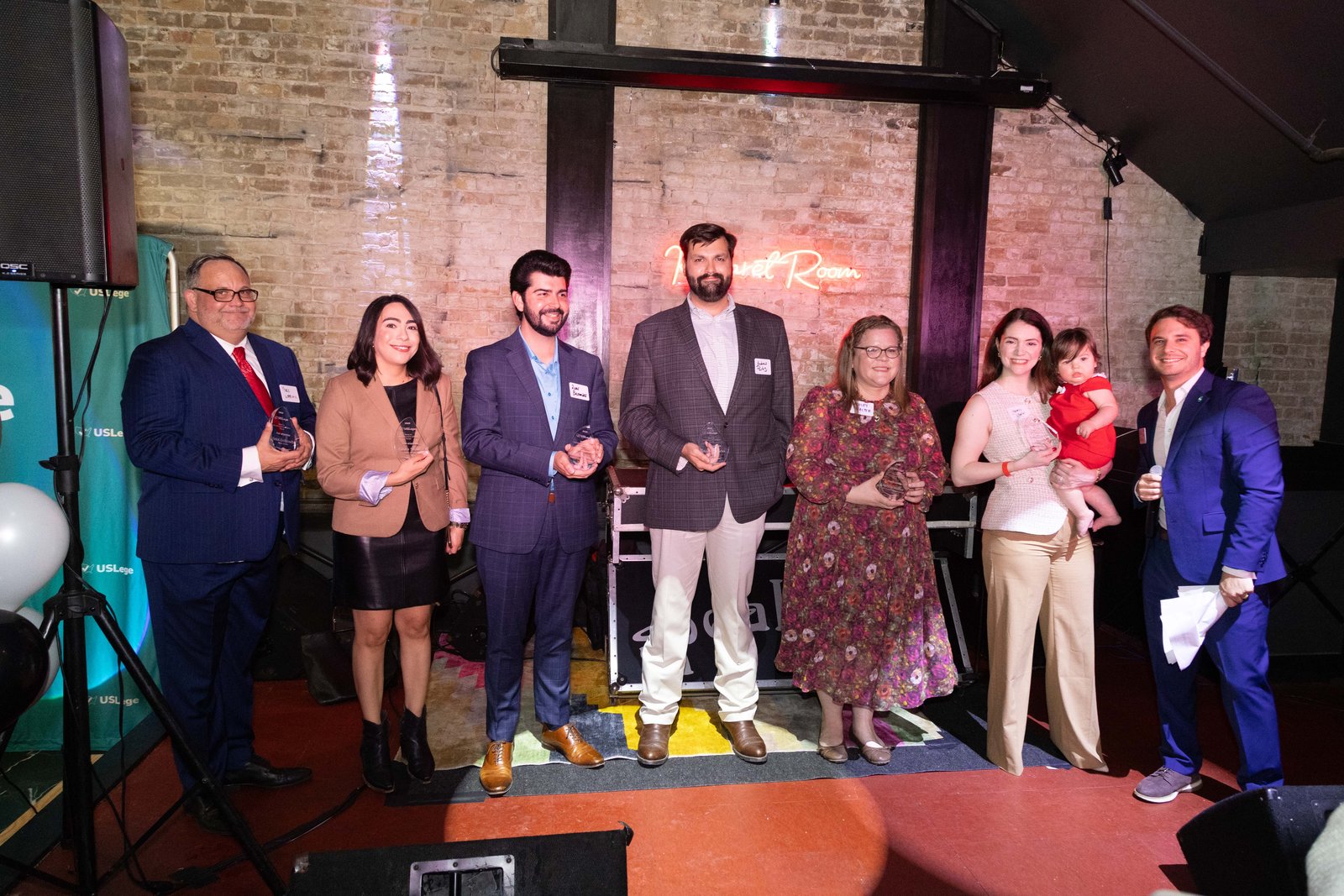 A group of award winners with trophies posing together on stage under the Kabaret Room sign
