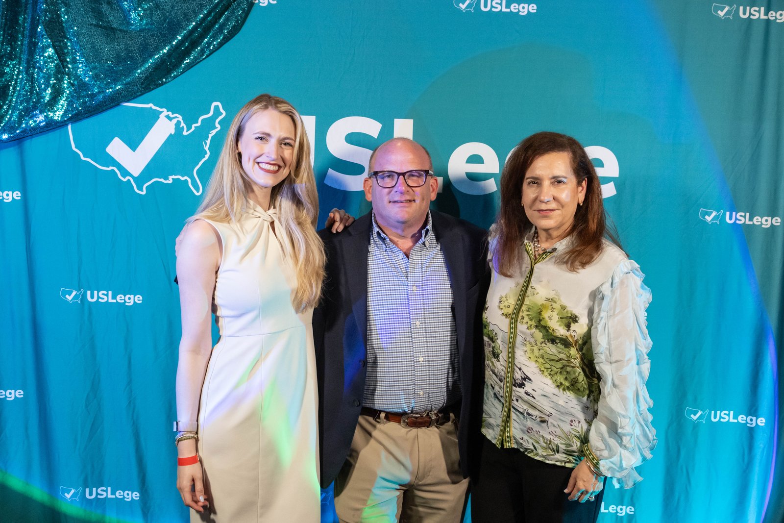 Laura Davis posing with two guests in front of the USLege step-and-repeat backdrop