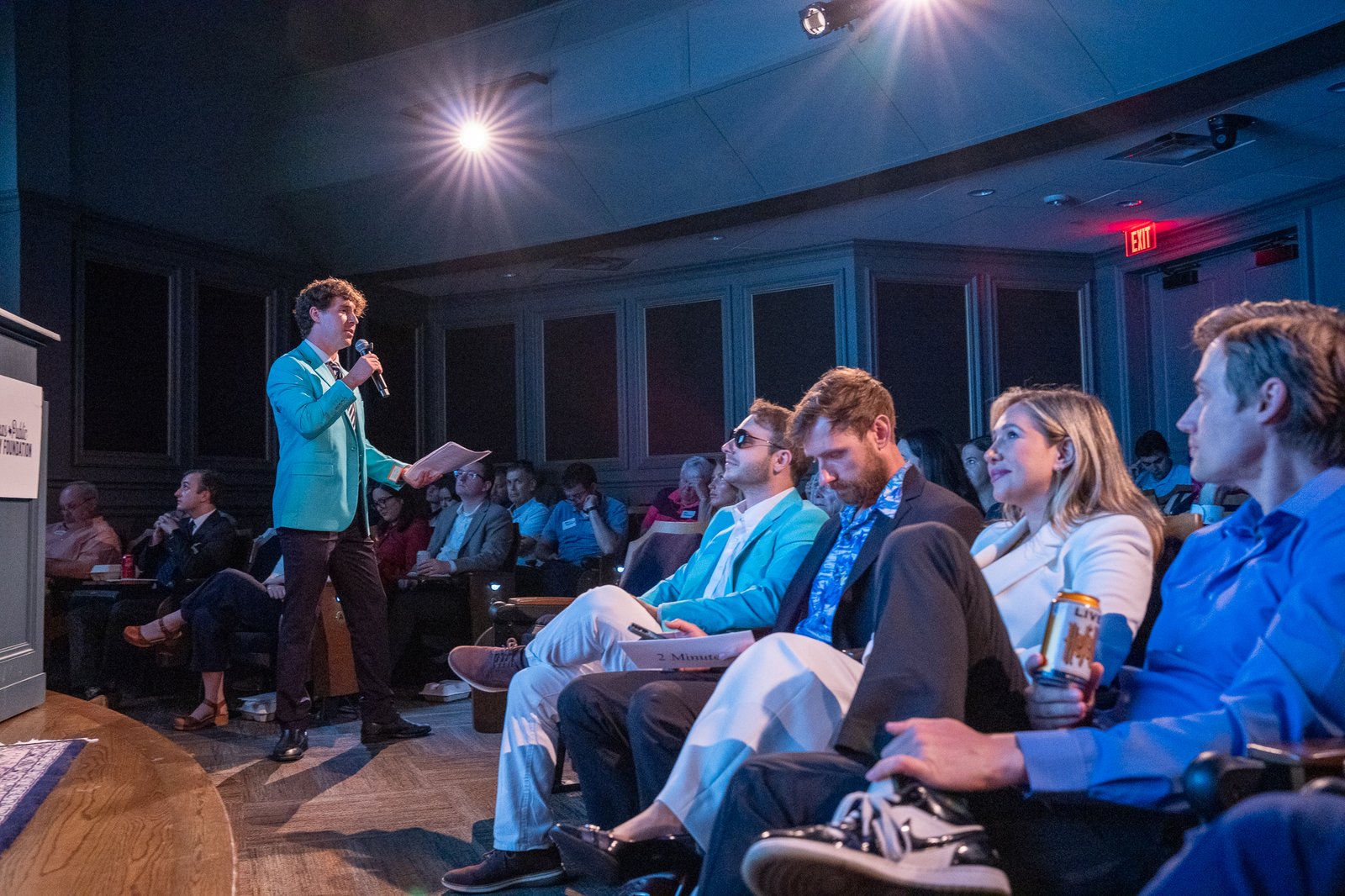 A presenter in a teal blazer speaking to the crowd during the pitch competition