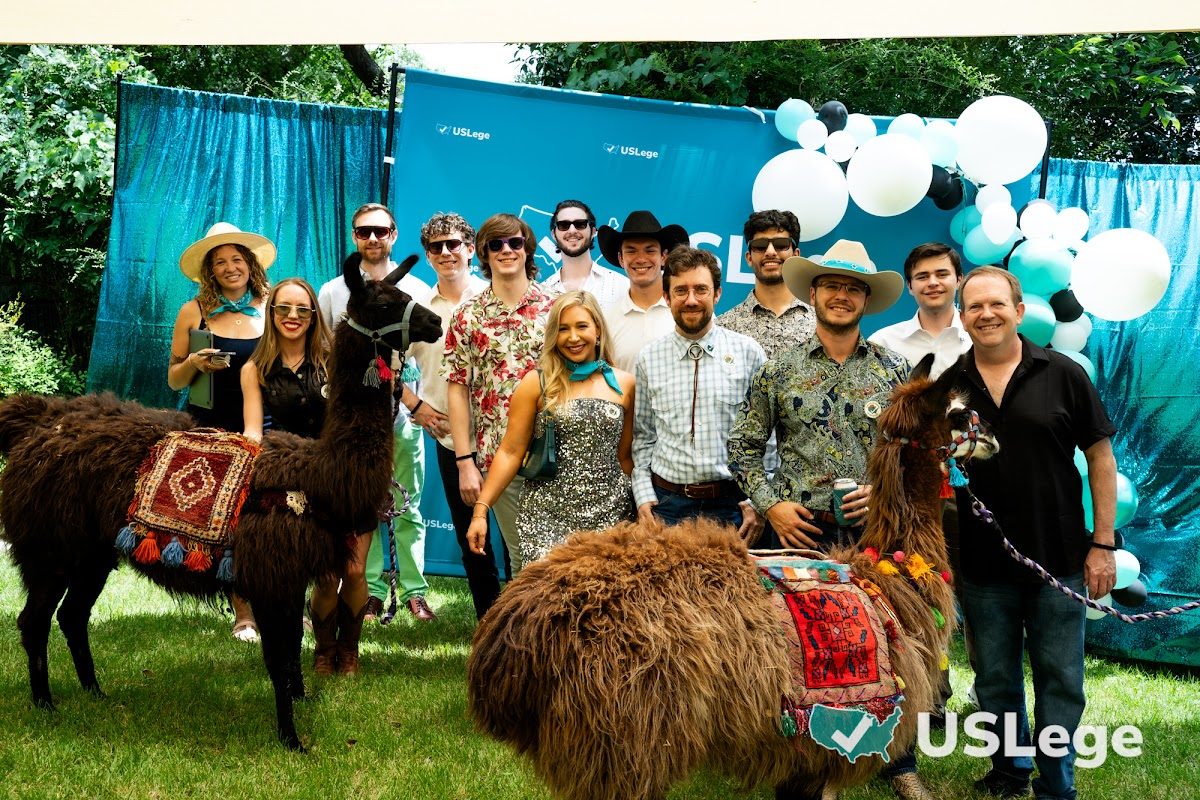 The USLege team posing with two llamas in front of a USLege balloon arch backdrop