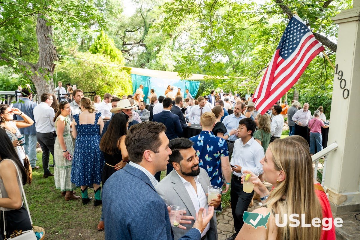 A large crowd of guests mingling at the Sine Die Celebration with an American flag overhead