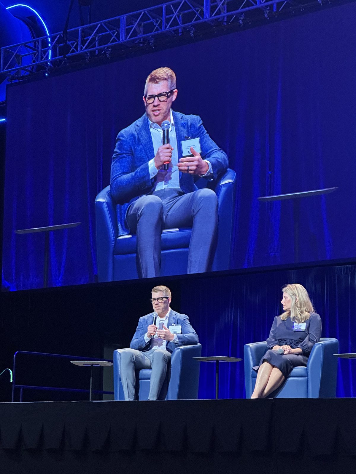 A fellow panelist speaking on the Texas Dynamism jumbotron, with Laura Davis seated at the end of the panel